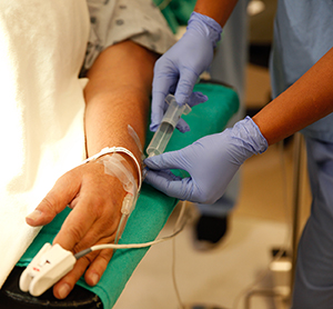 Primo piano di un operatore sanitario mentre inietta farmaci in endovena nella mano di un uomo.