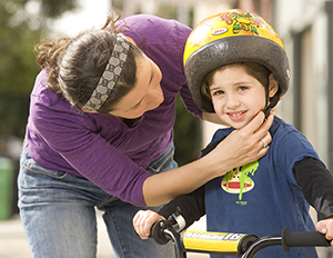 Una donna che fa indossare il casco da bicicletta a un bambino in età prescolare.